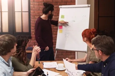 A person giving a presentation on a white board, with a curious audience